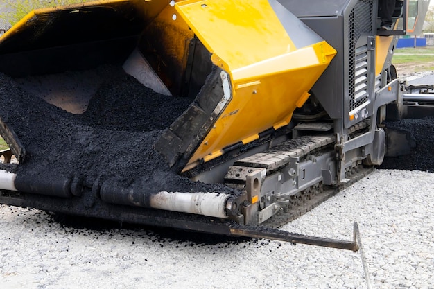 Worker operating asphalt paver machine during road construction and repairing works