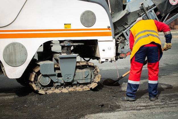 Worker in an orange uniform with a shovel works near the milling machine