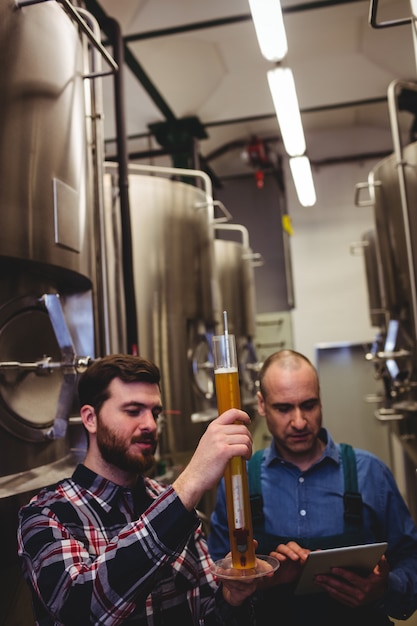 Worker and owner inspecting beer at brewery