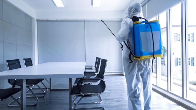 Photo worker in personal protective equipment ppe suit cleaning in building with spray disinfectant water to remove covid 19