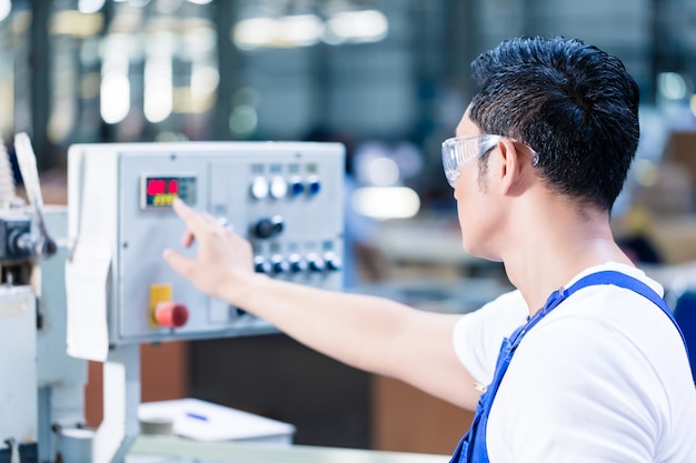 Worker pressing buttons on CNC machine control board in Asian factory