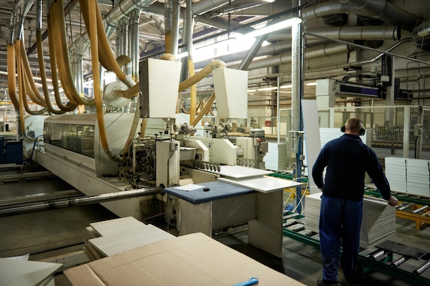 A worker processes furniture blanks on a complex technological machine at a factory. Industrial production of furniture.