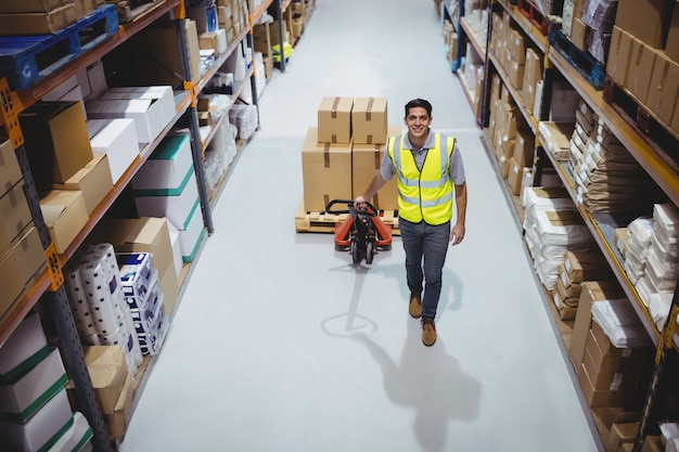 Worker pulling trolley with boxes in warehouse