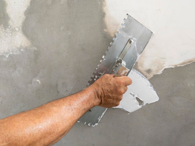 Photo worker puts finishing layer of stucco on the wall using a plastering trowel