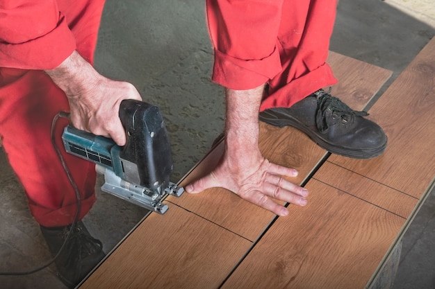 Photo a worker in a red jumpsuit cuts a laminate with a electric jigsaw by saws the bar