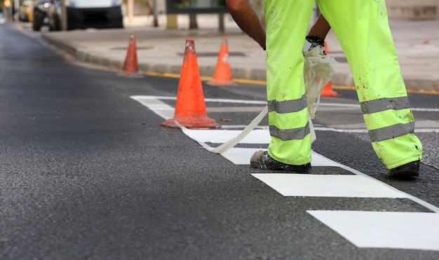 worker in reflective pants removes thermoplastic marking tape from road works to paint traffic lines