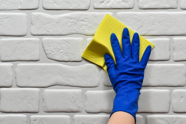 Worker's hand in a rubber protective glove with a rag wiping the surface of a table or wall in a room bathroom kitchen Early spring or regular cleaning