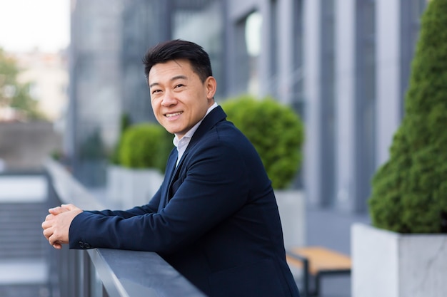 Worker salesman asian businessman, on the balcony of a modern office center, man in a business suit cheerful and happy smiling