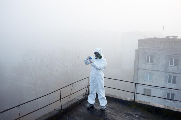 Worker scientist wearing protective coverall and gas mask doing ecological tests on the roof