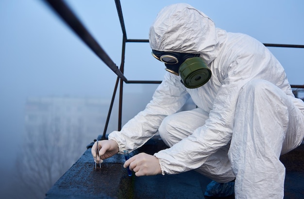 Worker scientist wearing protective coverall and gas mask doing ecological tests on the roof