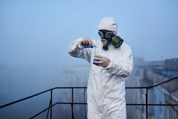 Worker scientist wearing protective coverall and gas mask doing ecological tests on the roof