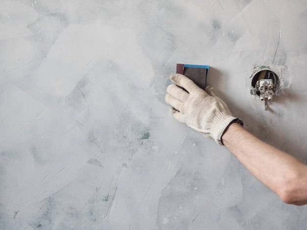 Worker scrubbing the wall with sandpaper and prepare the surface for painting. Repair and renovation at home. New interior design.