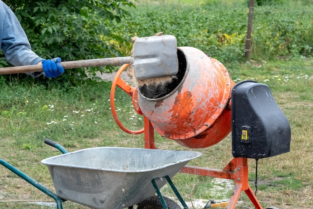 A worker shovels sand into a concrete mixer preparing cement mortar