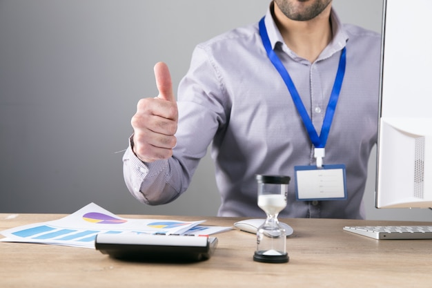 Worker showing thumb up while sitting at his desk .