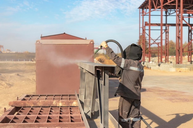 A worker in special clothing is sandblasting a metal building structure at an industrial site Industrial metal processing