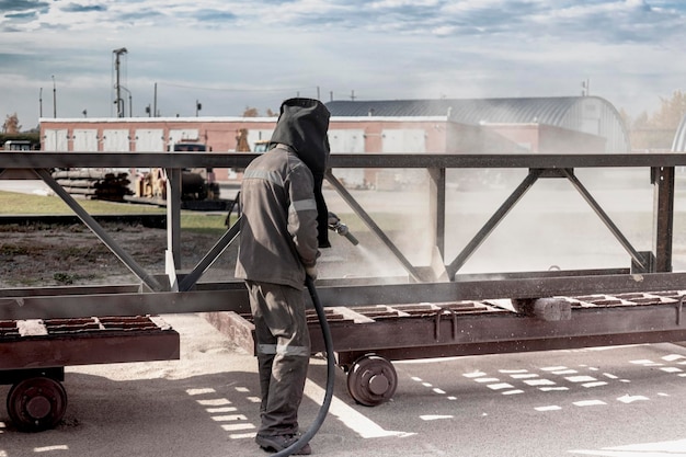 A worker in a special suit is sandblasting metal at an industrial site.