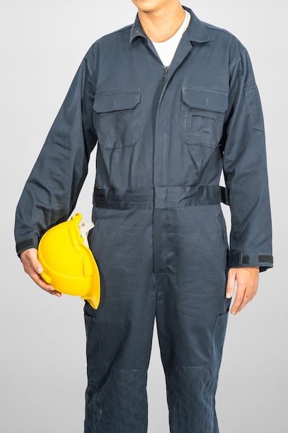 Worker standing in blue coverall holding yellow hardhat isolated on gray background