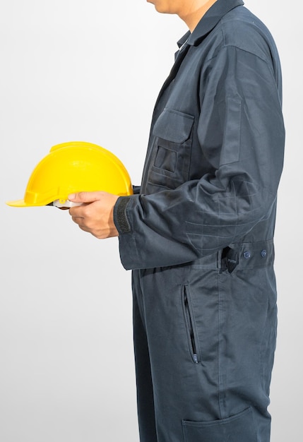 Worker standing in blue coverall holding yellow hardhat isolated on gray background