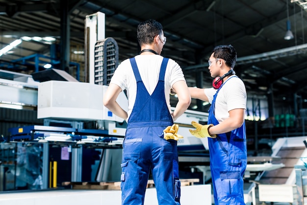 Worker team in factory discussing in front of machine