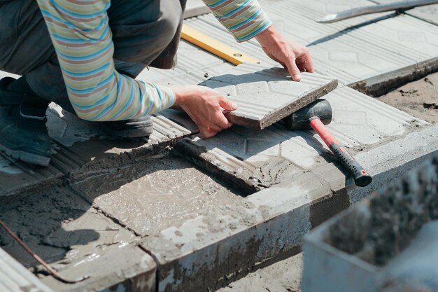 Worker tiler lays tiles with cement outside on summer day Authentic workflow Hands with facing tiles