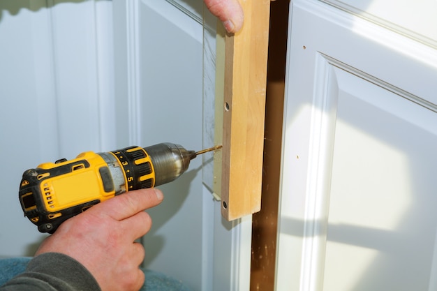 Worker use drill to repair furnitureand drills the cabinet door