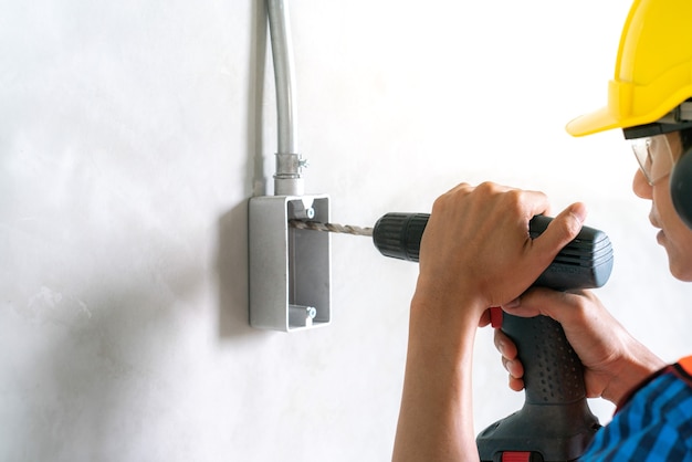 Worker use electric drill screwdriver to fix in electric junction box in renovate home bui