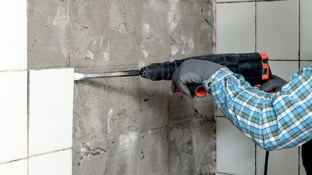 A worker uses a perforator to dismantle facing tiles in a bathroom