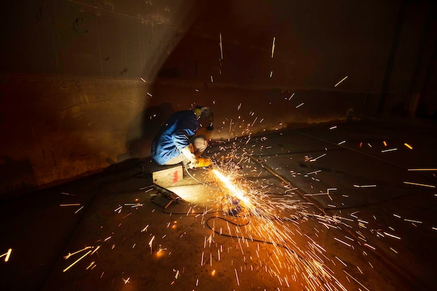 Worker using electric wheel spark grinding on welder metal carbon steel part bottom plate inside tank