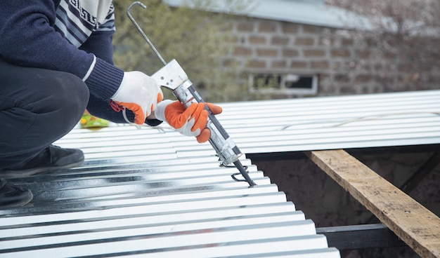 Worker using glue gun with adhesive to fix the metal steel on the roof