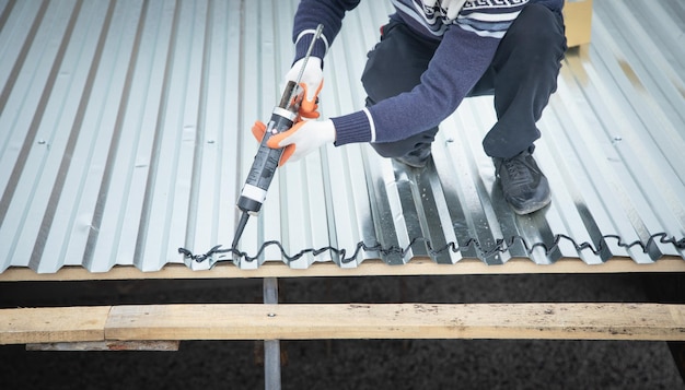 Worker using glue gun with adhesive to fix the metal steel on the roof