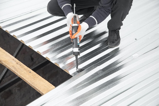 Photo worker using glue gun with adhesive to fix the metal steel on the roof