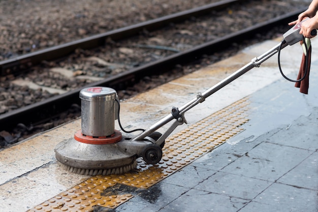 Worker using scrubber machine for cleaning and polishing floor. Cleaning maintenance train at railway station.