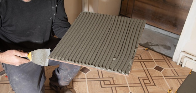 Worker using spatula and putting glue on ceramic tile