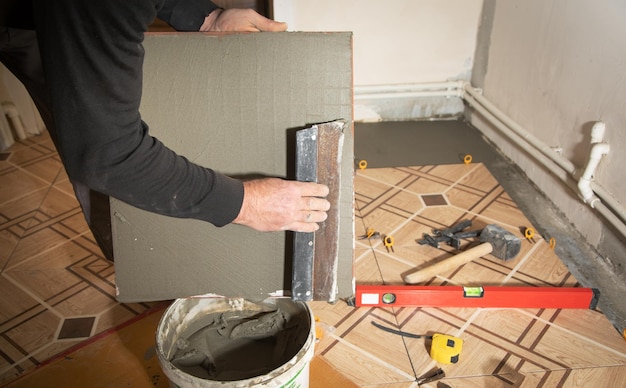 Worker using spatula and putting glue on ceramic tile