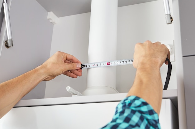 Worker using tape measure while installing new furniture in kitchen. carpenter assembles and installs furniture.