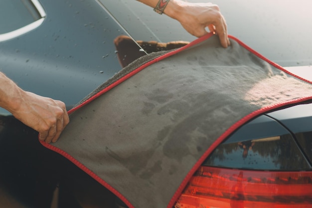 Worker washing car at car wash and wipes vehicle with rag