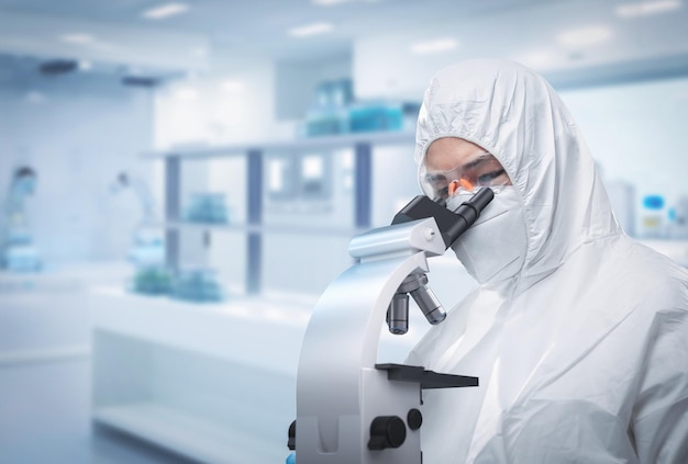 Worker wears medical protective suit or white coverall suit look through microscope