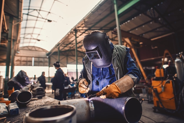 Worker welding iron. Protective suit and mask on. Workshop interior.