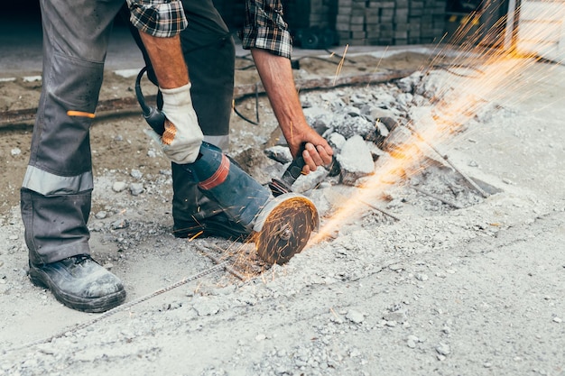 A worker with an angle grinder cuts the concrete pavement of the road and sparks fly