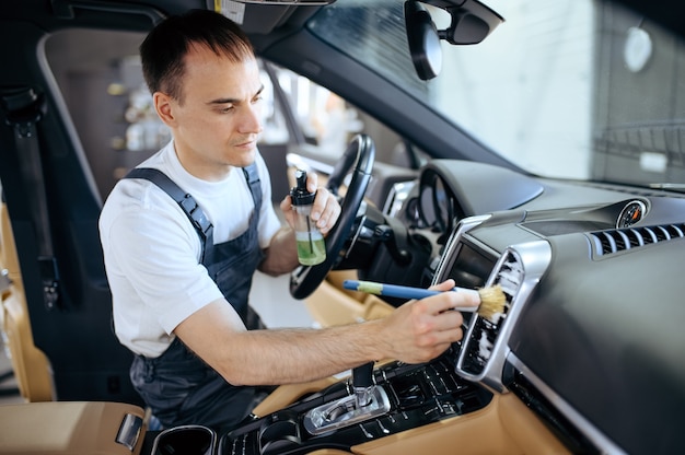 Worker with brush wipes car air duct grating, dry cleaning and detailing