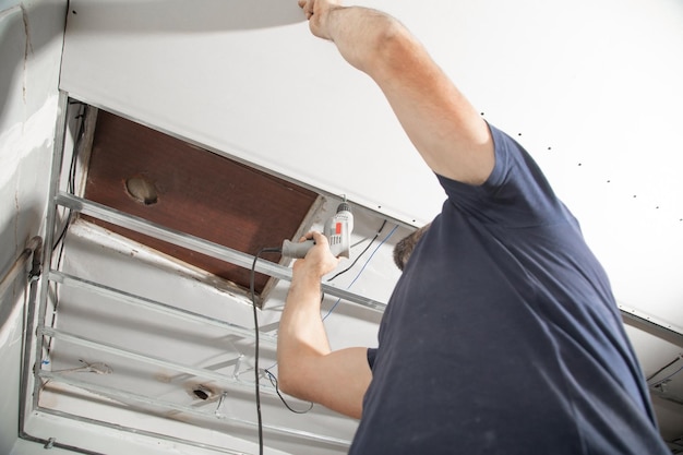 Worker with a drill screwdriver twists the screw into the drywall