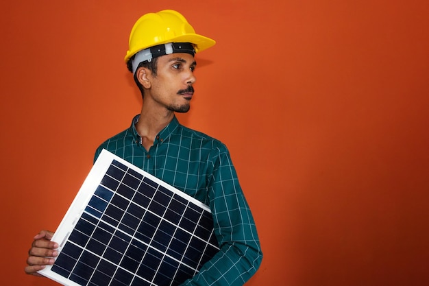 Worker With Helmet and Individual Protection Equipment Holding a Solar Photovoltaic Panel isolated Solar Worker isolated in orange background