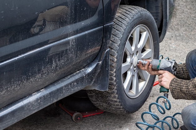 Worker with a pneumatic wrench unscrews the bolts from the car wheel