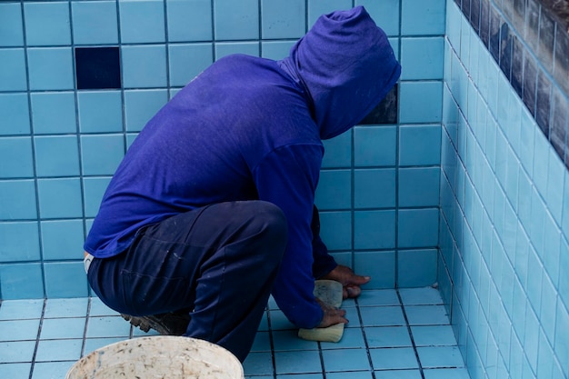 Worker with sponge cleaning pool to apply grout between tiles