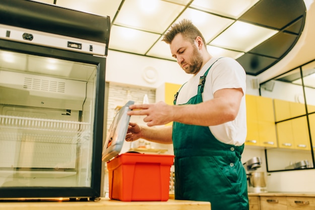 Worker with toolbox repair refrigerator at home. Repairing of fridge occupation, professional service