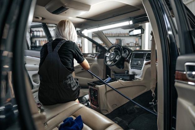 Worker woman vacuum cleaning dust interior inside car in car wash