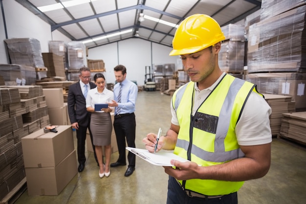 Worker writing on clipboard in front of his colleagues