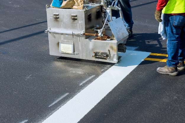 Photo workers apply a road marking to the stripe with white paint and sprinkle the stripes with a reflective powder on the new asphalt