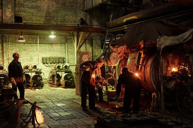 Workers in helmets working in team they melting iron in metal factory