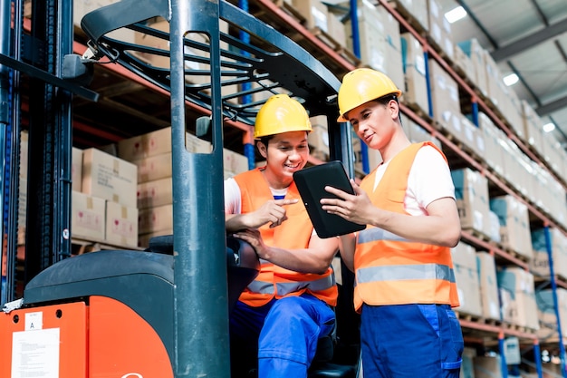 Workers in logistics warehouse at forklift checking list